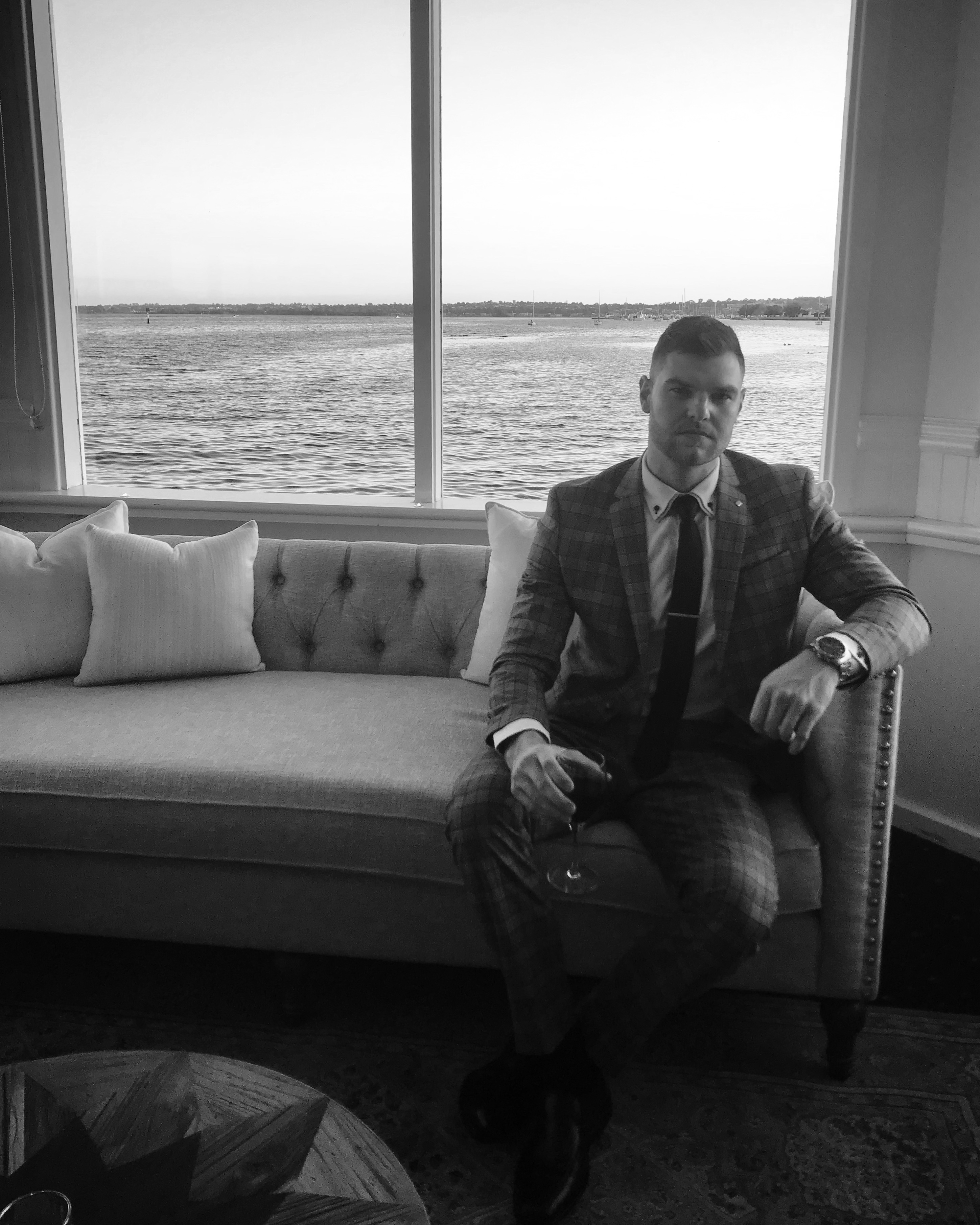 Bryce Huston in a suit beside a large waterfront window